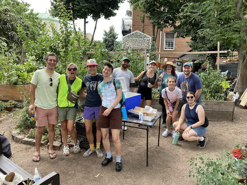 Ten volunteers posing for a photo in the garden with happy and silly expressions. There is a folding table behind them holding supplies for an event.